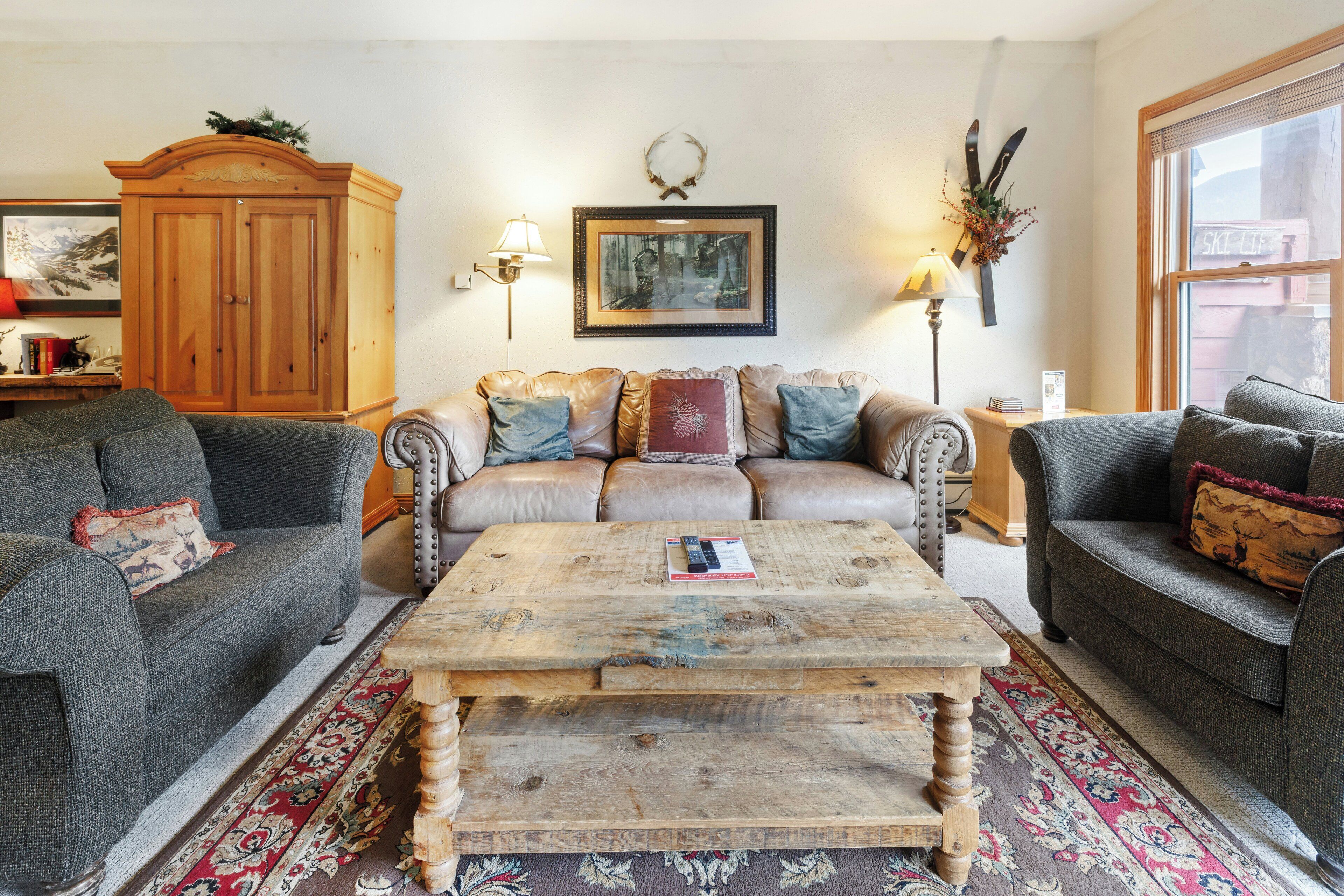 A cozy living room with a wooden coffee table, two sofas, a cabinet, and a large window.