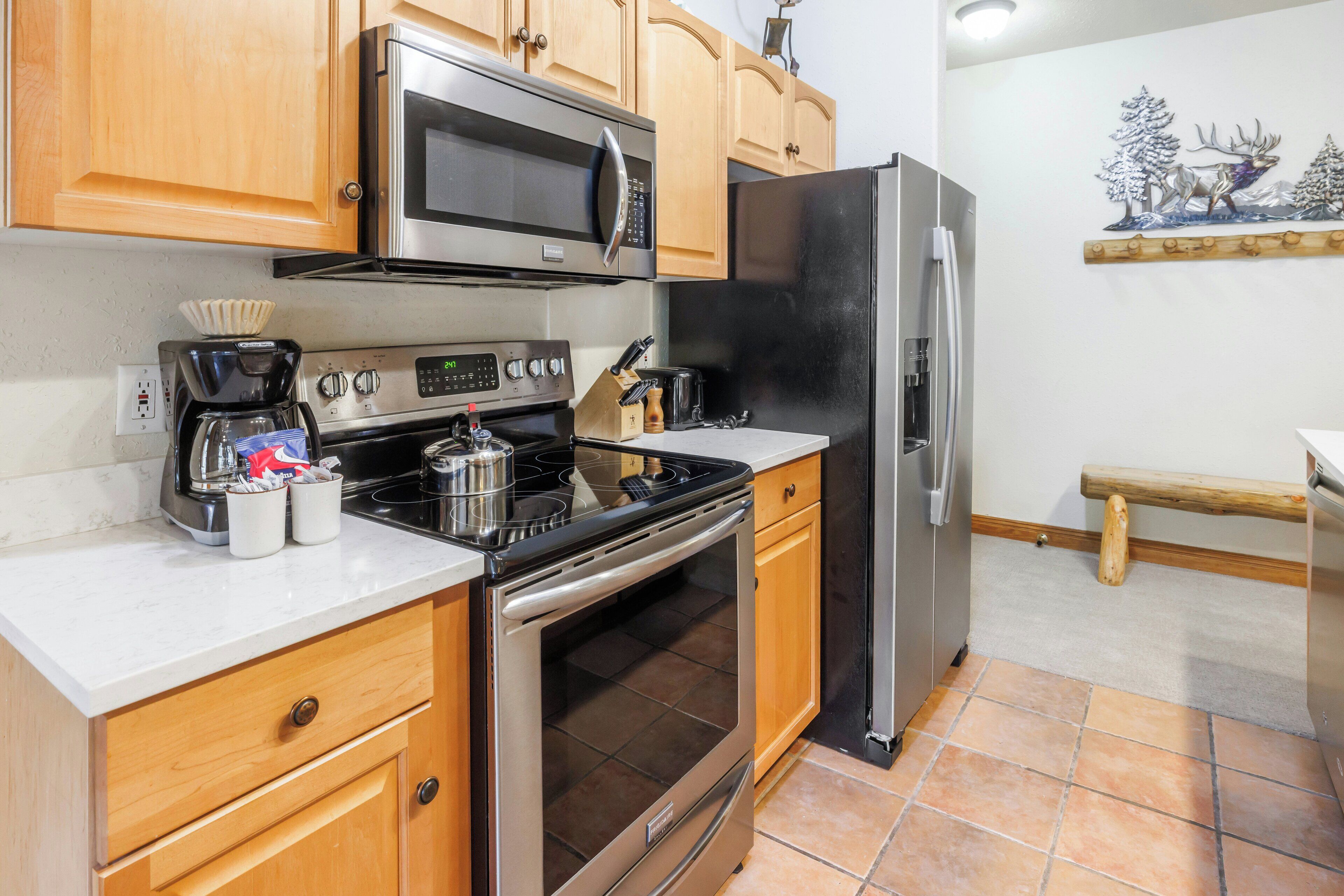 A kitchen with wooden cabinets, a stainless steel microwave, a black refrigerator, a stove, and a coffee maker.