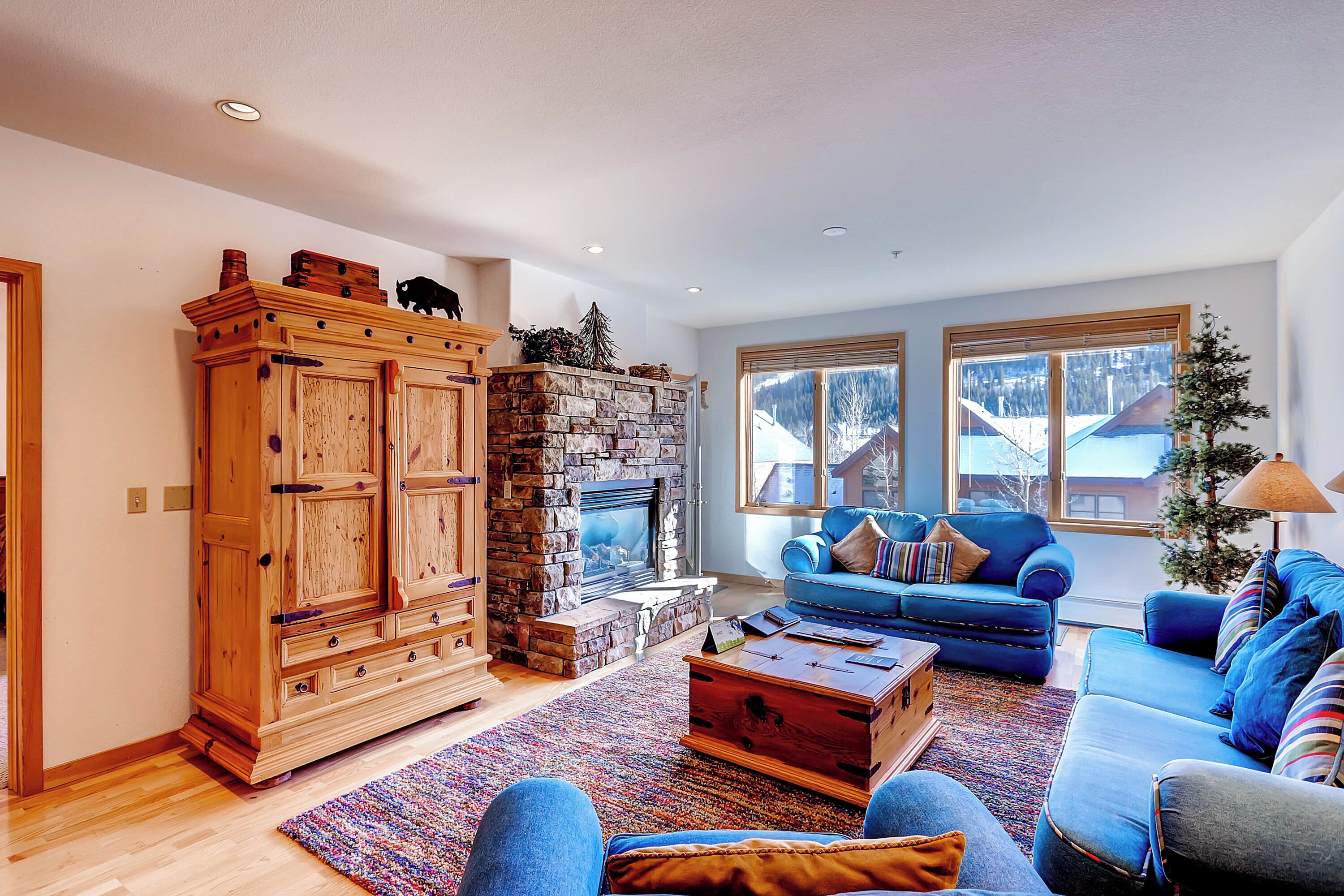 A spacious living room with a stone fireplace, a large wooden cabinet, and a blue sofa set.