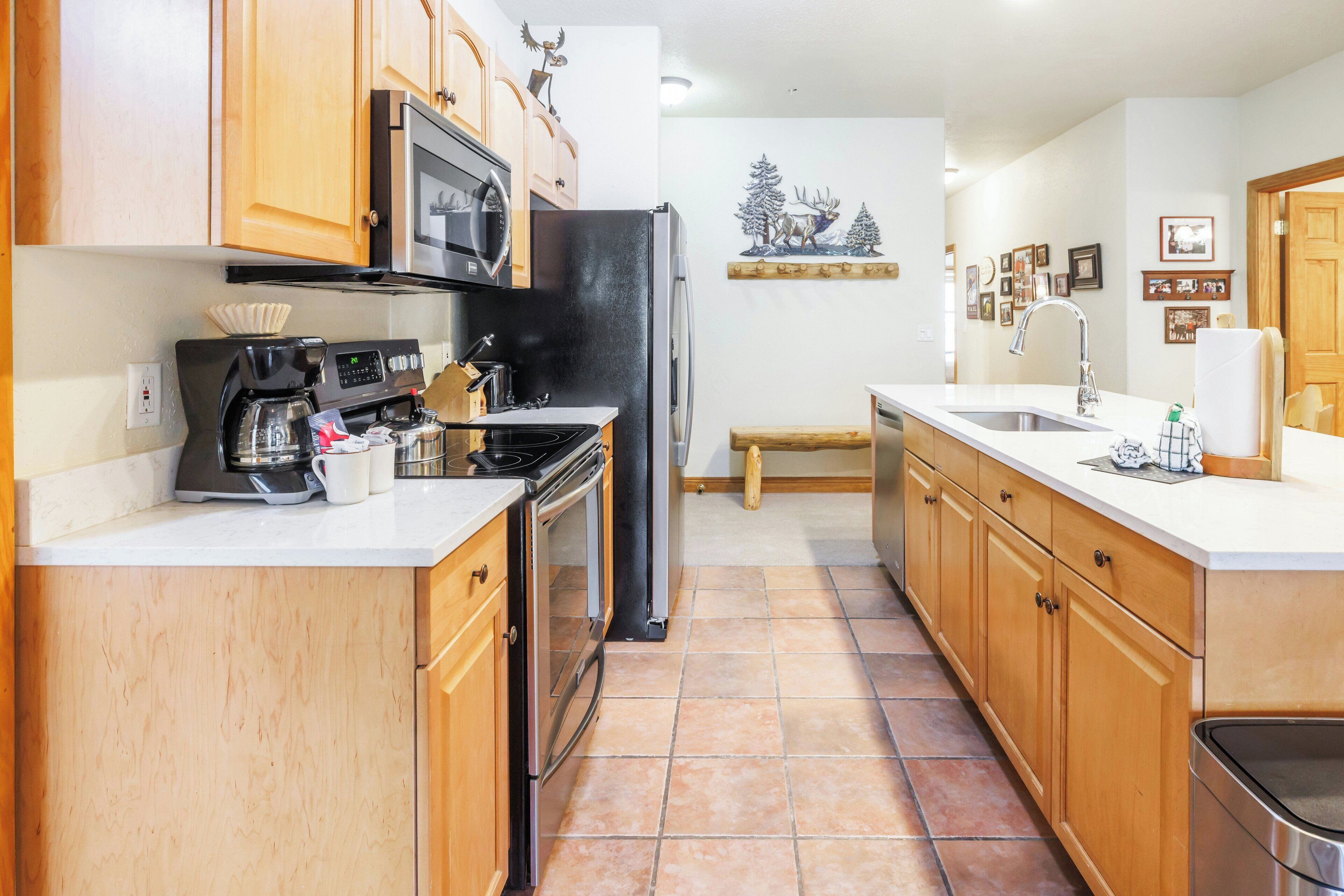 A kitchen with wooden cabinets, a black refrigerator, a microwave, a coffee maker, and a sink.