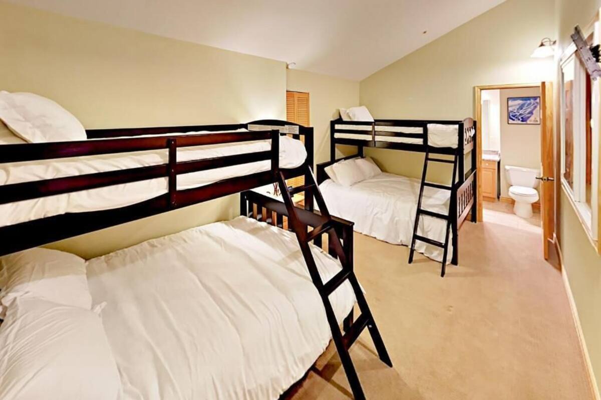 A room with bunk beds, a bathroom with a toilet and sink, and a door leading to another room.