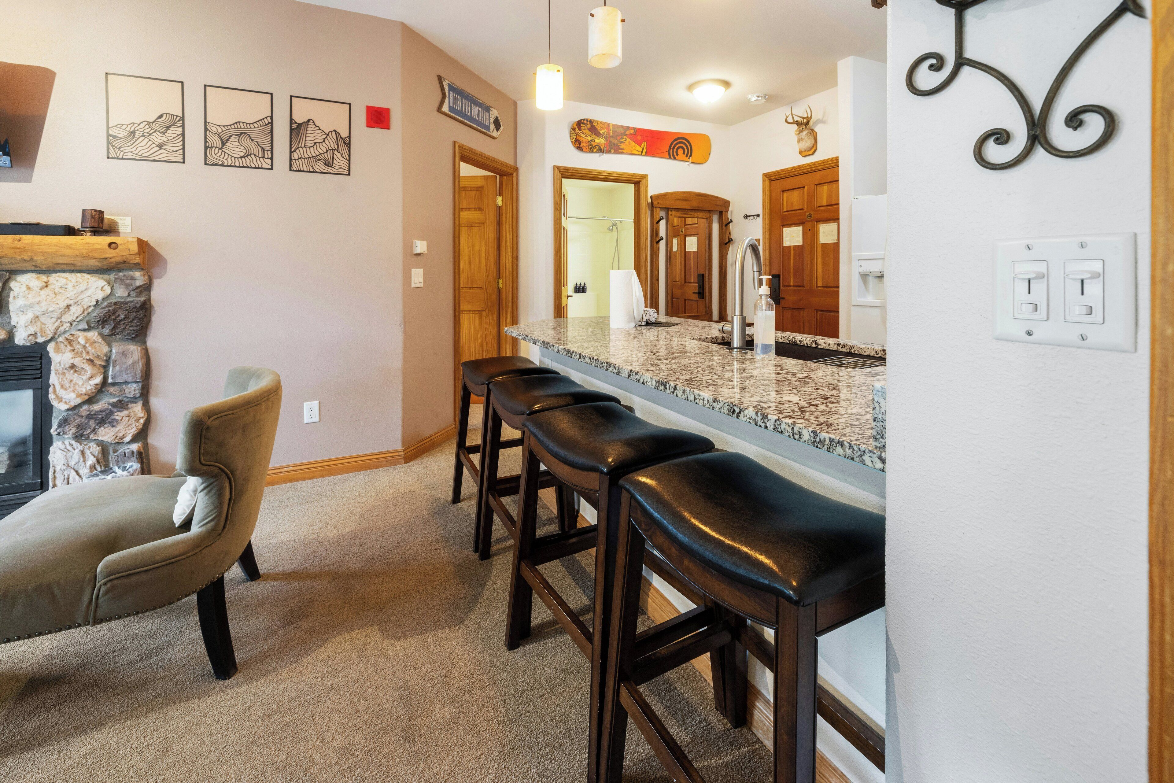 A kitchen with a stone fireplace, wooden bar stools, and a granite countertop.