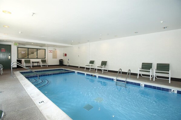 Una piscina interior con agua cristalina, un trampolín y varias sillas de descanso a lo largo de la piscina.