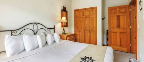 A neatly made bed with white linens and a beige throw, a wooden nightstand with a lamp, and a wooden wardrobe.