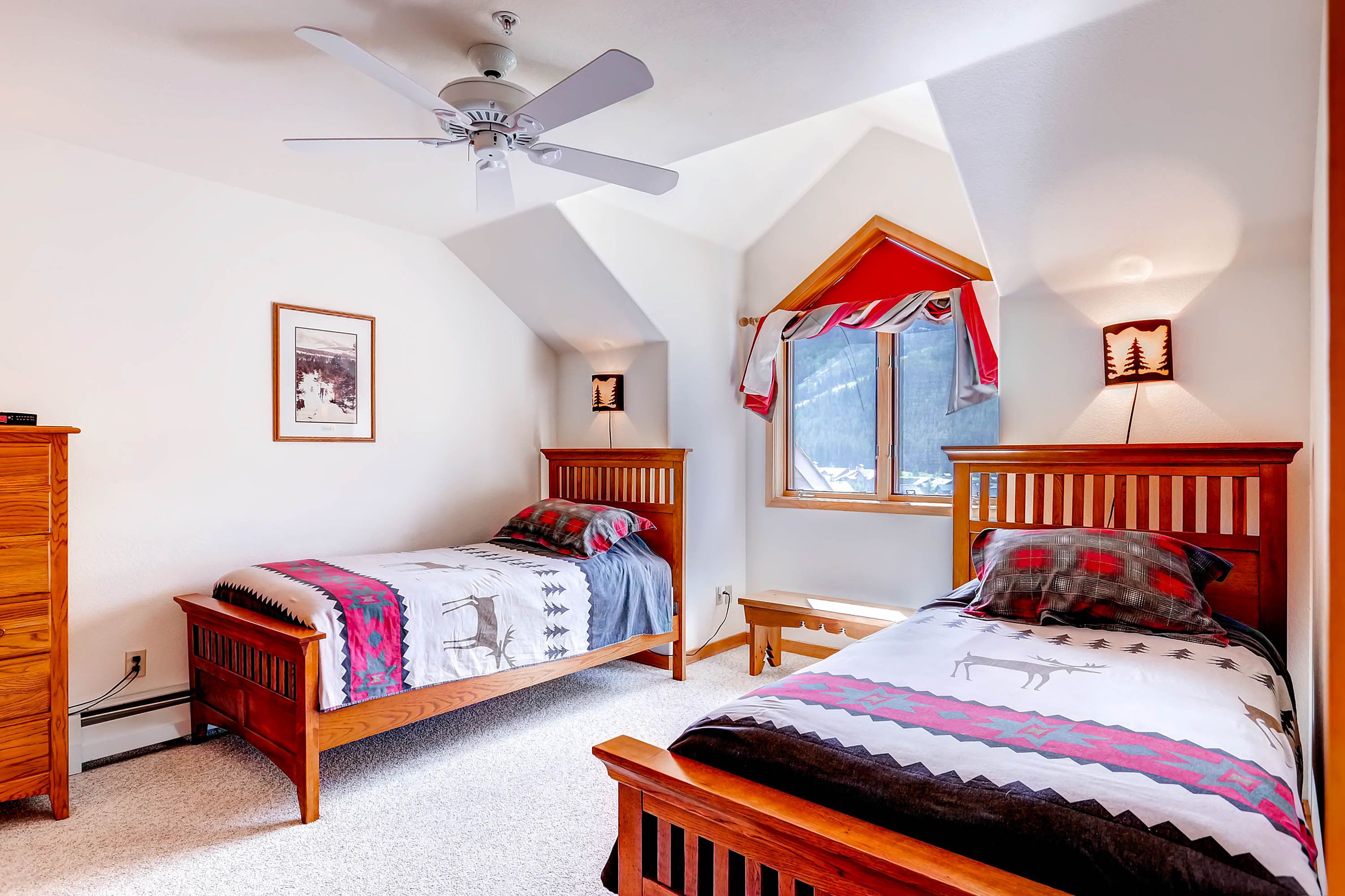 Ein Schlafzimmer mit zwei hölzernen Betten, einem Deckenventilator, einem Fenster mit Vorhängen und einer Wandleuchte.