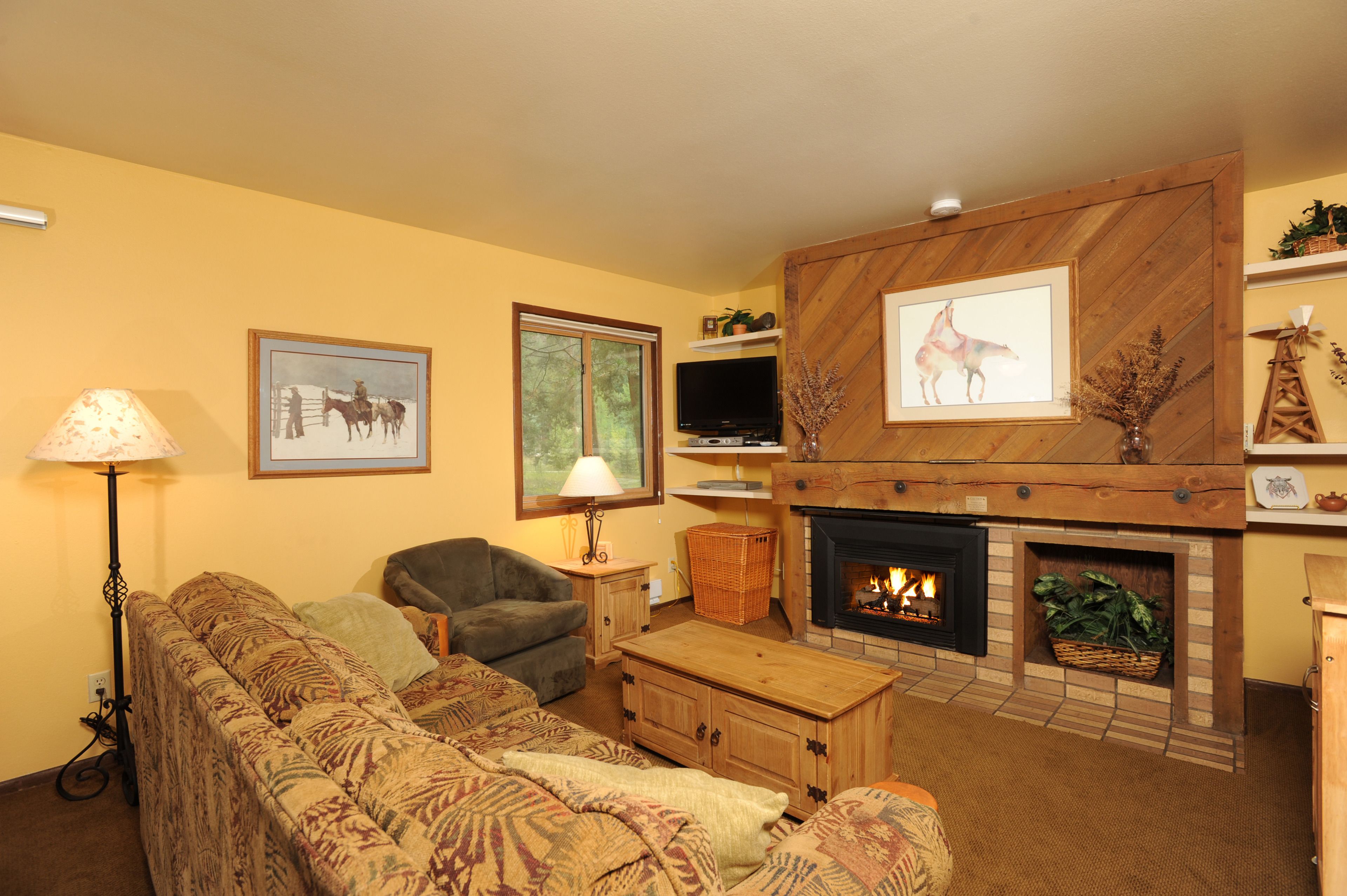 A cozy living room with a fireplace, a sofa, a television, and framed artwork on the walls.