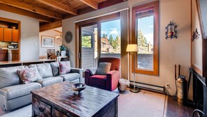 A cozy living room with a wooden ceiling, a sofa, a red armchair, and a view of the outside. - Aspen Ridge Condominiums by Vail Resorts (Keystone)