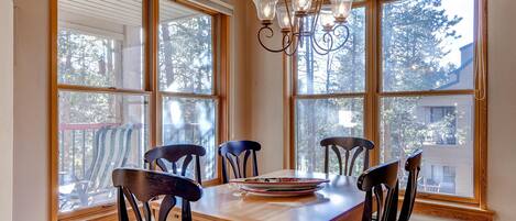 Un espace repas avec une table et des chaises en bois, de grandes fenêtres et un lustre.