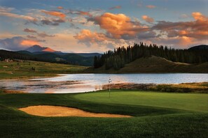 A golf course with a water body, a flagstick, and a mountain in the background. - Aspen Ridge Condominiums by Vail Resorts (Keystone)