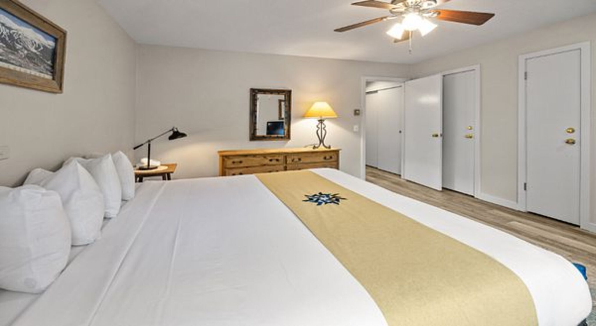 Una habitación de hotel con cama, mesita de noche, lámpara, cómoda y ventilador de techo.