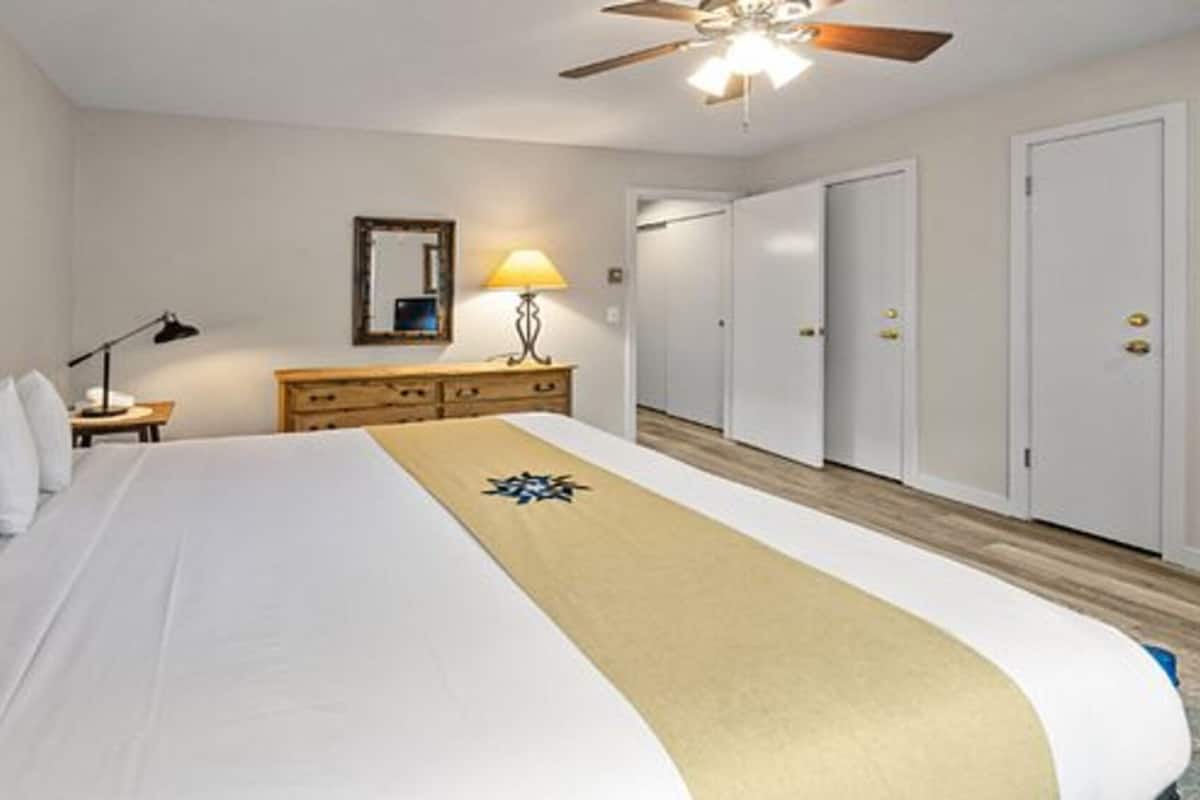 A hotel room with a bed, a nightstand, a lamp, a dresser, and a ceiling fan.