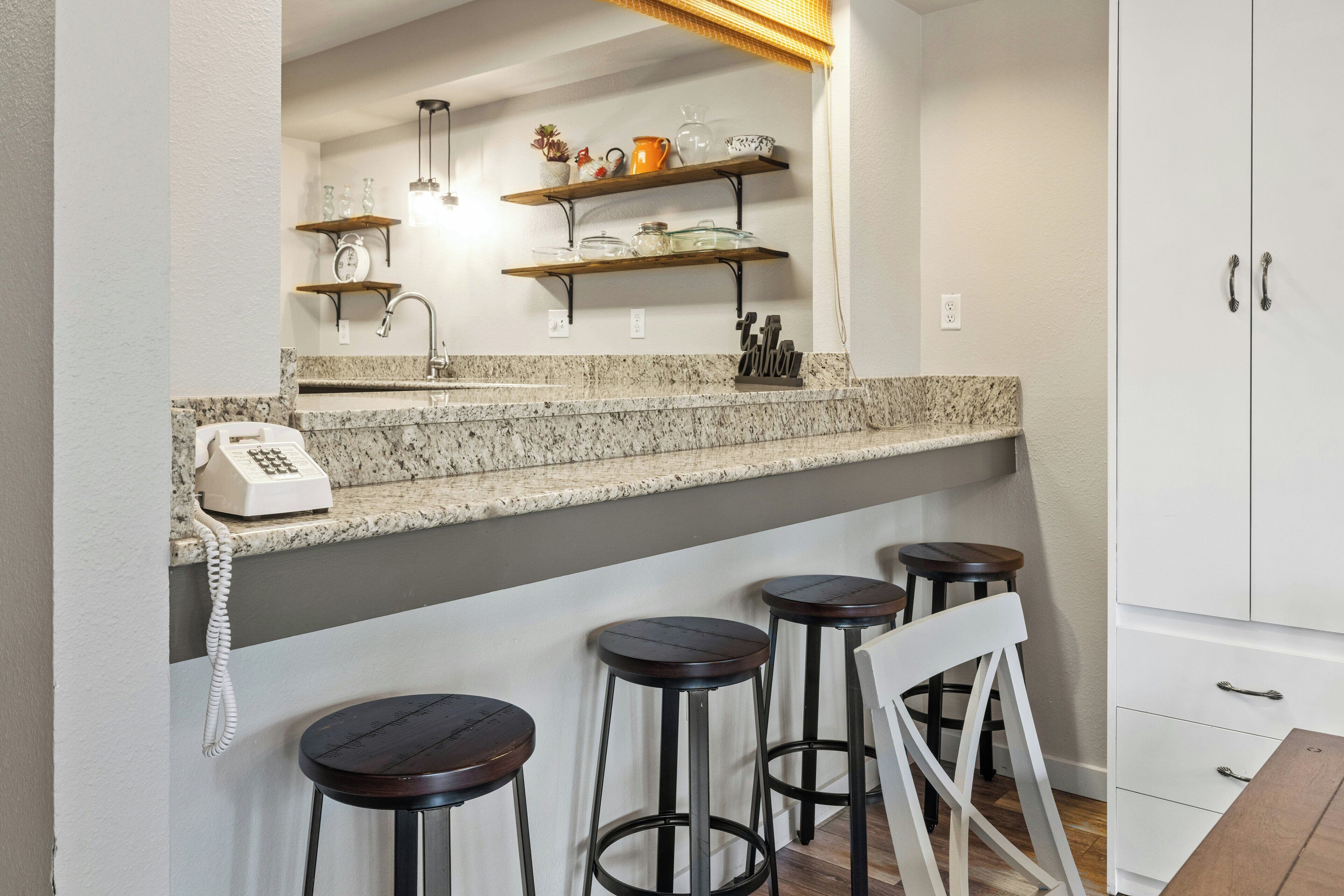 A kitchen with a granite countertop, a built-in phone, and three bar stools.