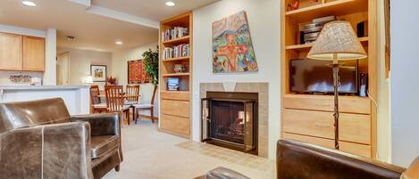A living room with leather sofas, a fireplace, a bookshelf, and a dining area in the background.