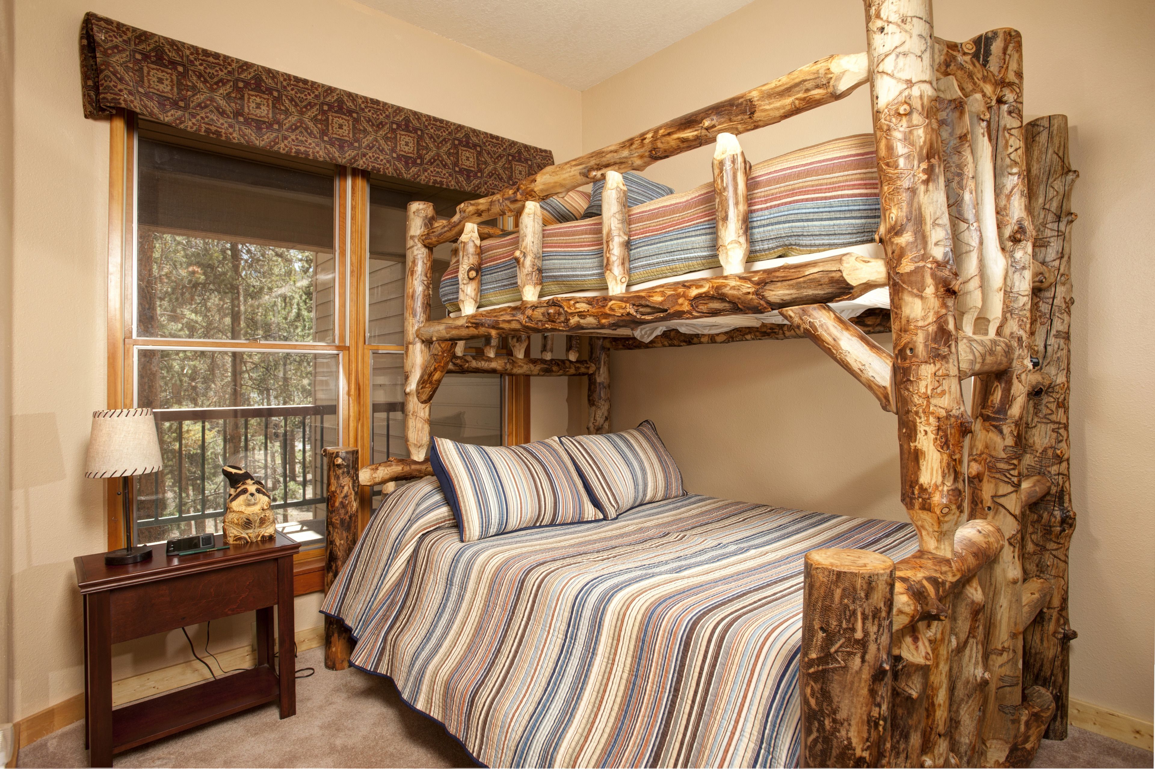 A rustic wooden bed with a slatted headboard, a striped bedspread, and a bedside table with a lamp.