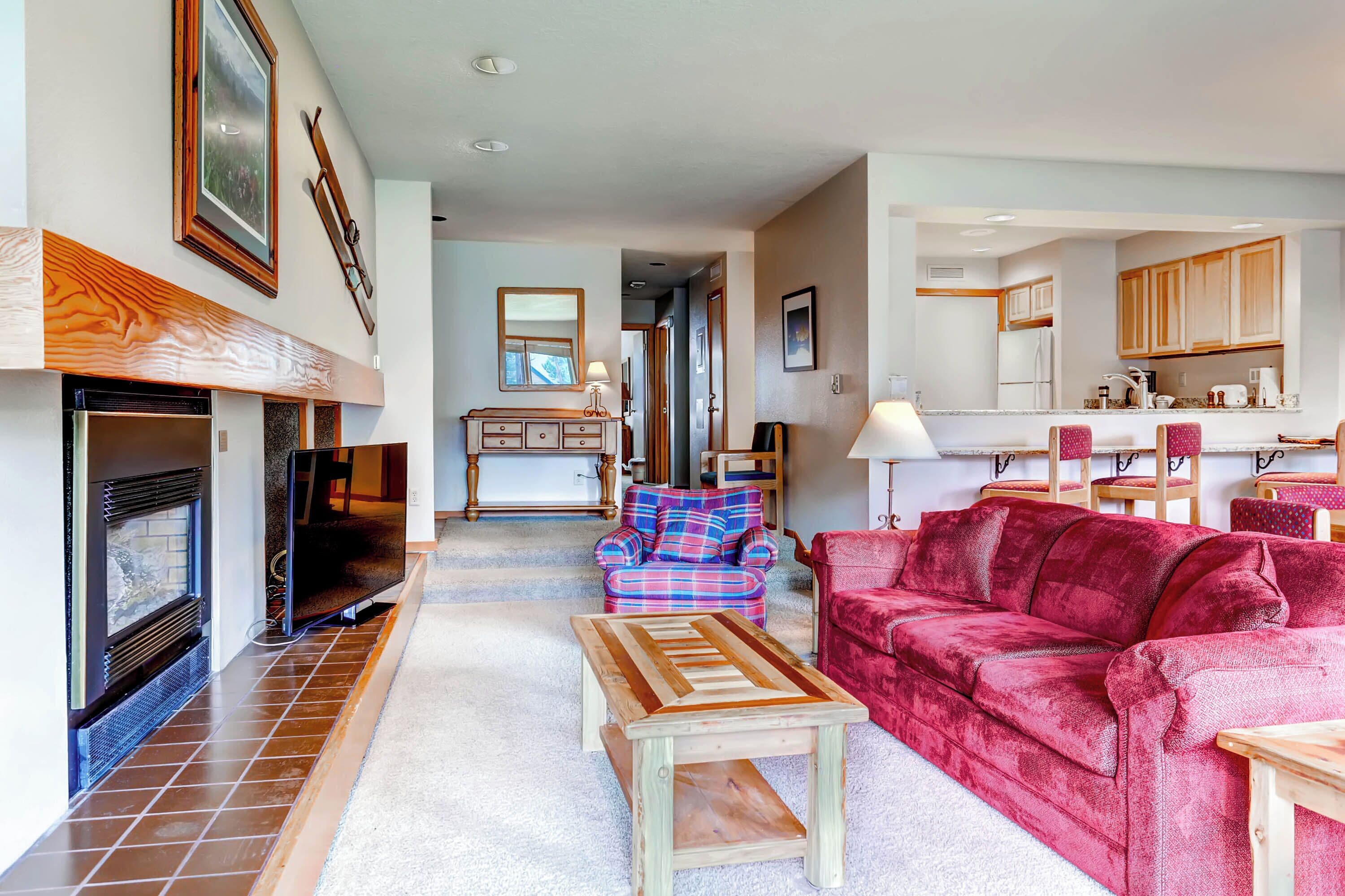 A living room with a fireplace, a television, a red sofa, a blue plaid sofa, and a wooden coffee table.