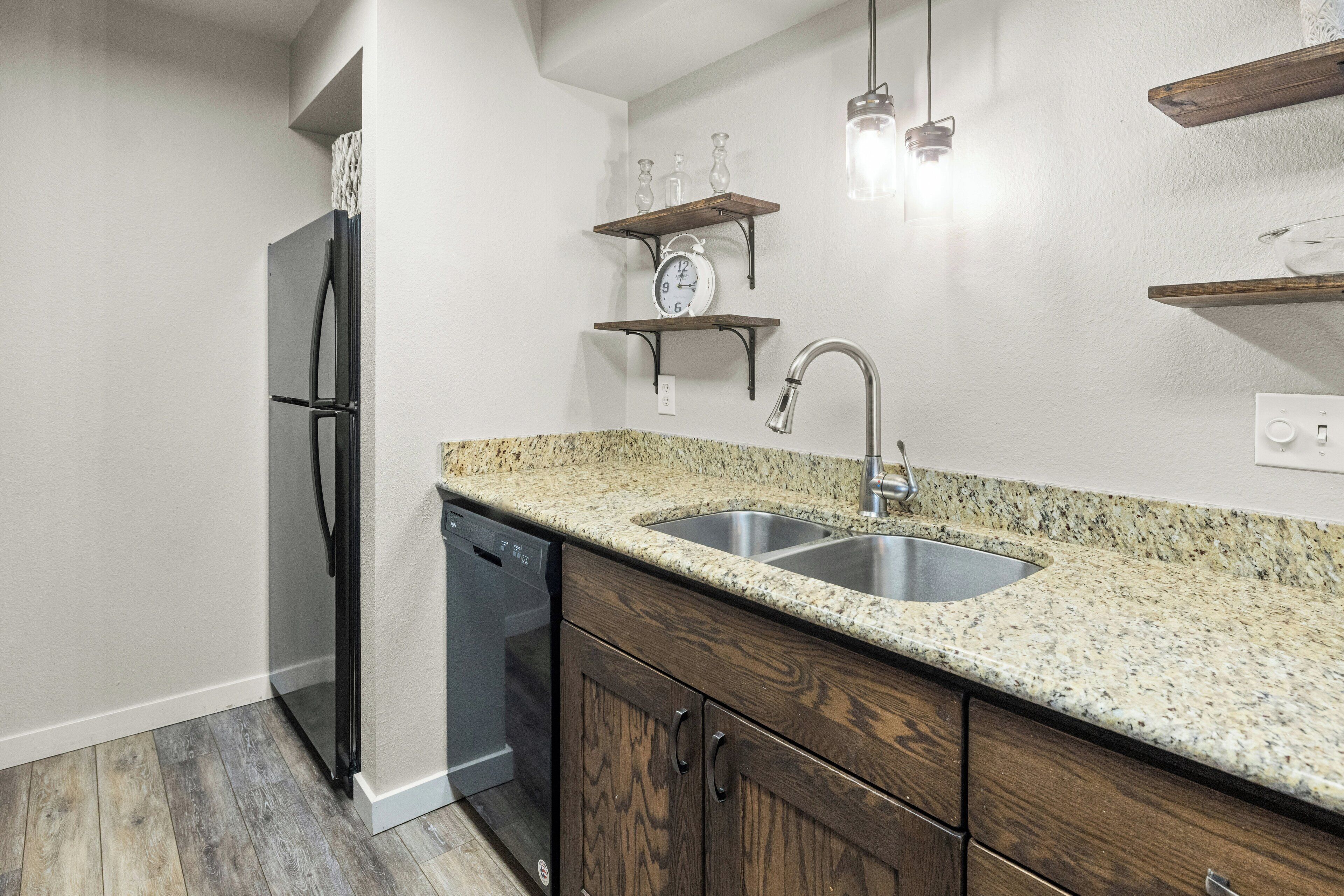 A kitchen with granite countertops, a stainless steel sink, wooden cabinets, and a built-in dishwasher.