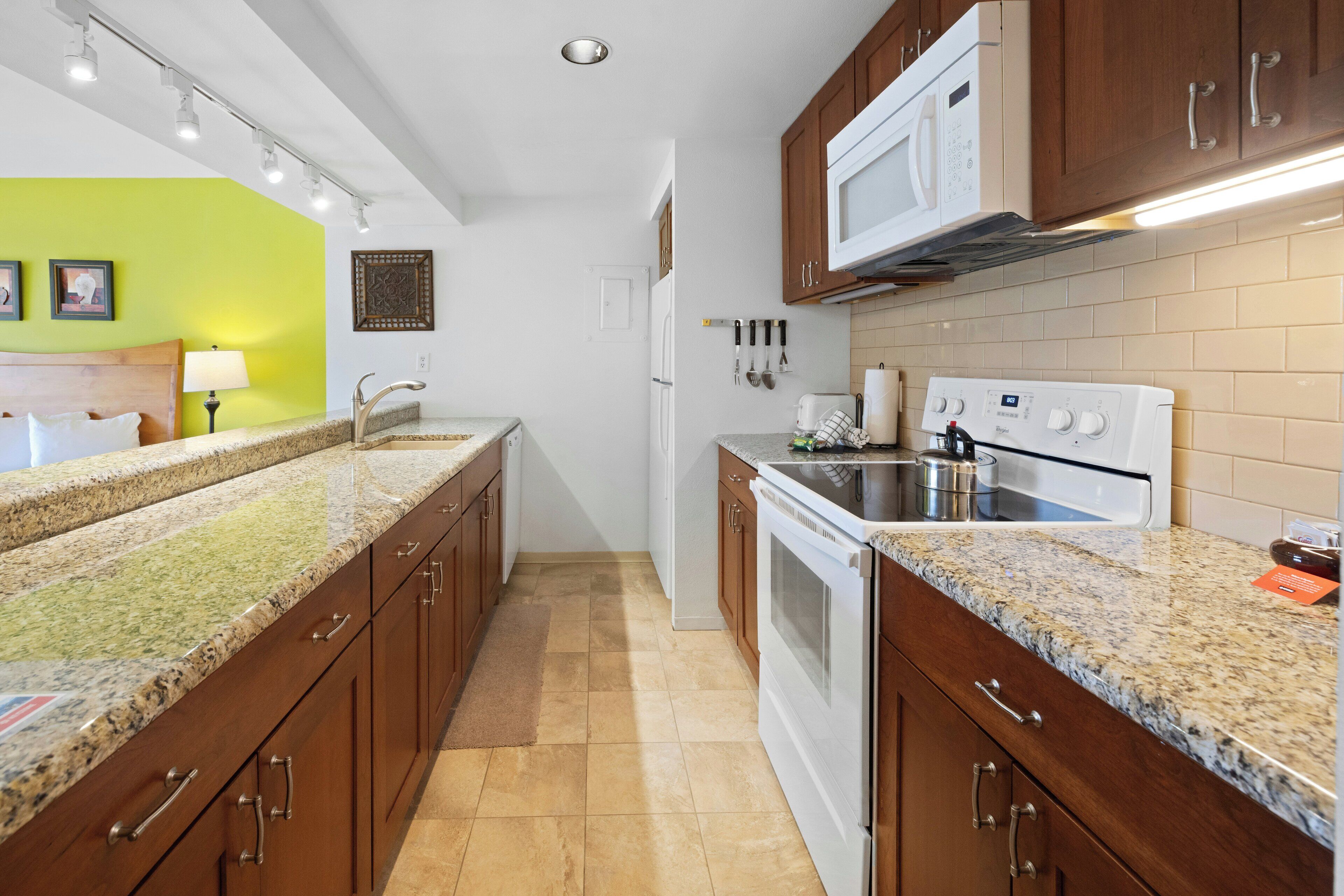 Une cuisine dotée de plans de travail en granit, de meubles en bois, d’une cuisinière blanche et d’un four à micro-ondes.