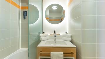 A bathroom with a white sink, wooden vanity, and a glass shower enclosure.