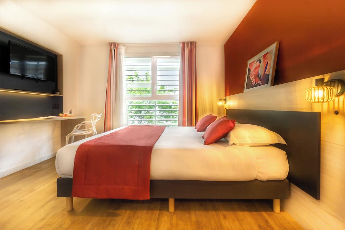 A modern hotel room with a large bed, a flat-screen TV, a bedside table, and a window with curtains.