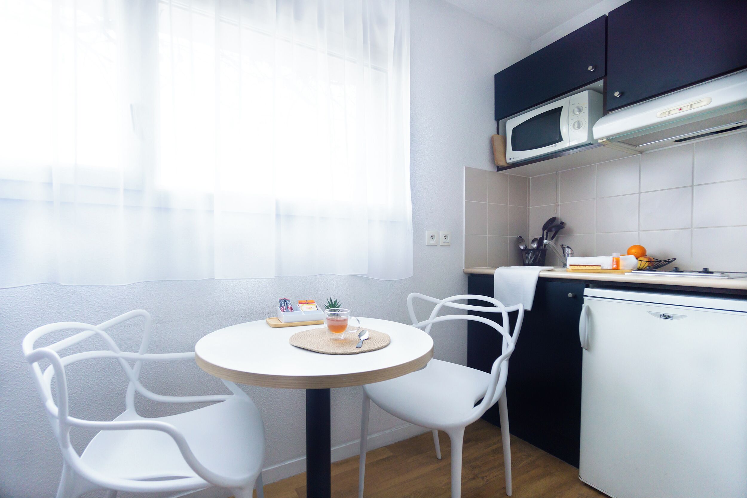 A small kitchen with a microwave, a refrigerator, and a dining area with two chairs and a table.