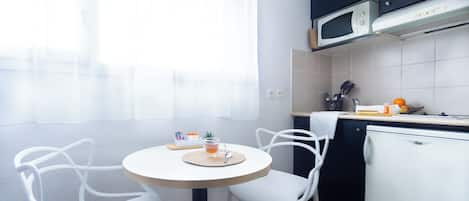 A small kitchen with a microwave, a refrigerator, and a dining area with two chairs and a table.