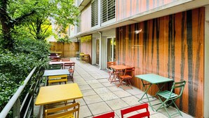 An outdoor café area with tables and chairs, a wooden fence, and a building with striped walls. - City Résidence Bordeaux Centre (Bordeaux)