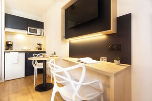 Una cocina compacta con microondas, cafetera y un pequeño comedor con sillas blancas y una mesa de madera.