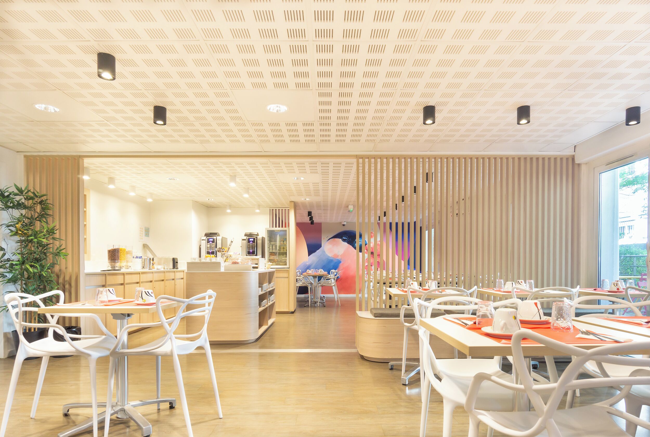 A modern dining area with white chairs and tables, a wooden counter, and a large window.