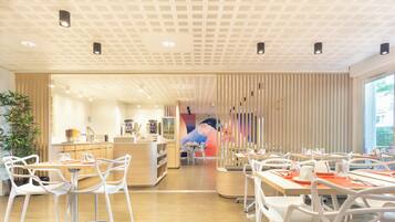 A modern dining area with white chairs and tables, a wooden counter, and a large window.