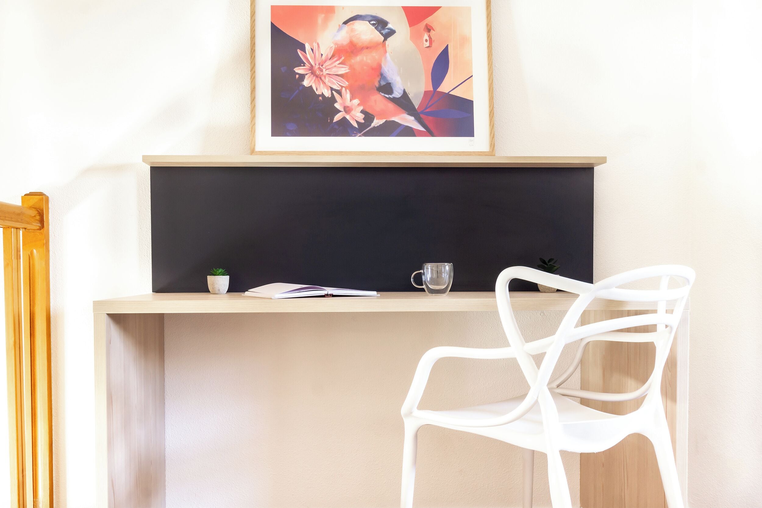 A desk with a framed painting, a potted plant, a notebook, and a cup.