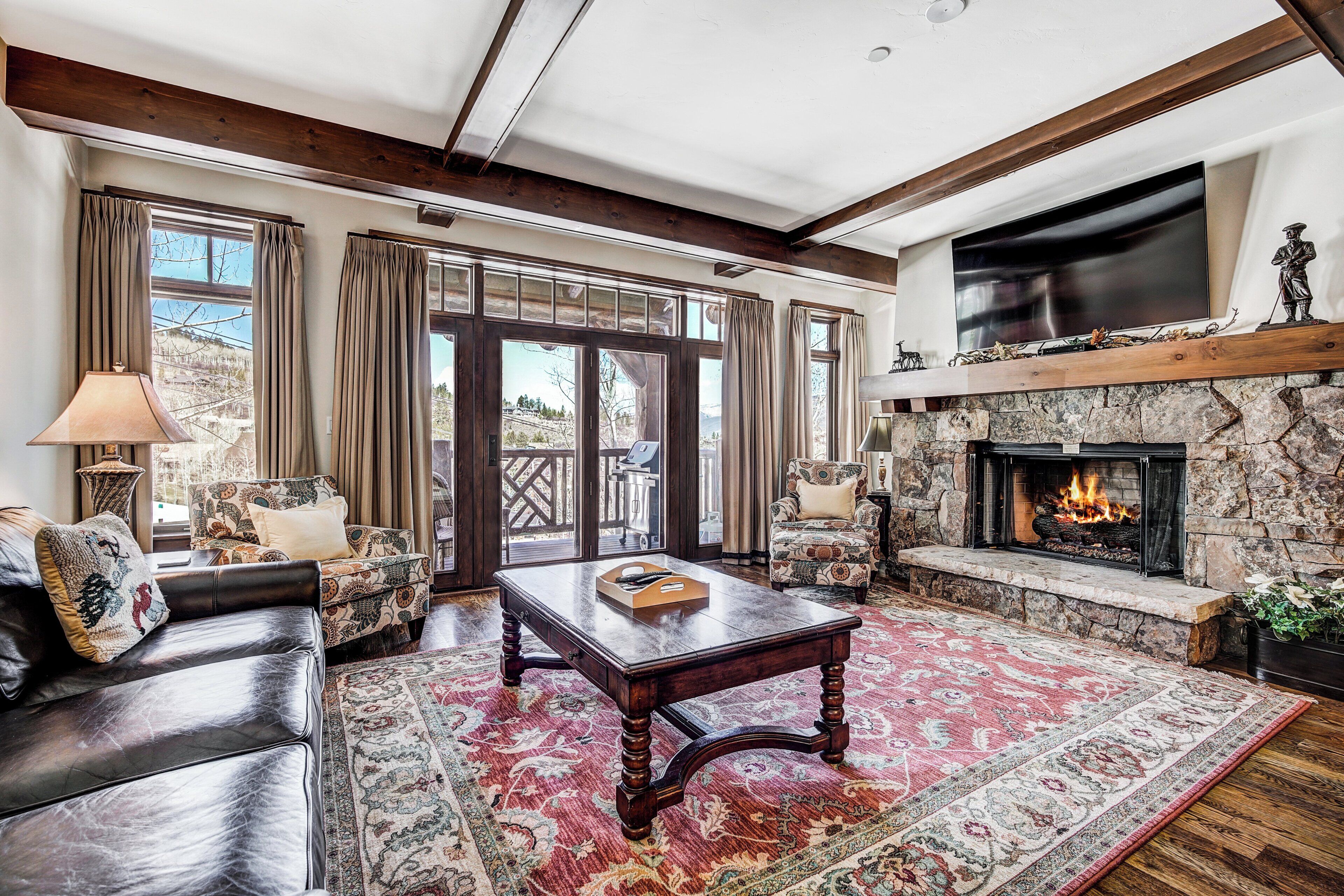 A living room with a fireplace, leather sofas, a coffee table, and a large window with curtains.