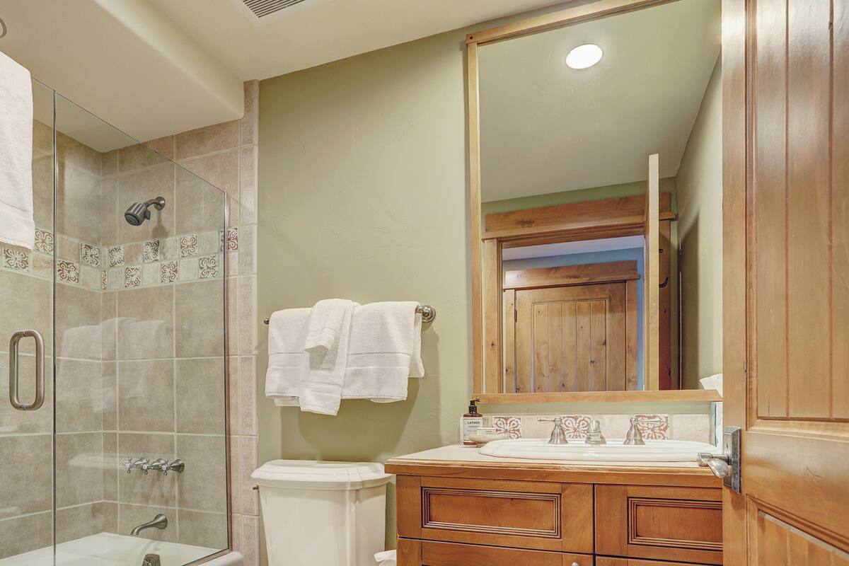 A bathroom with a glass shower enclosure, a wooden vanity with a mirror, and a toilet.
