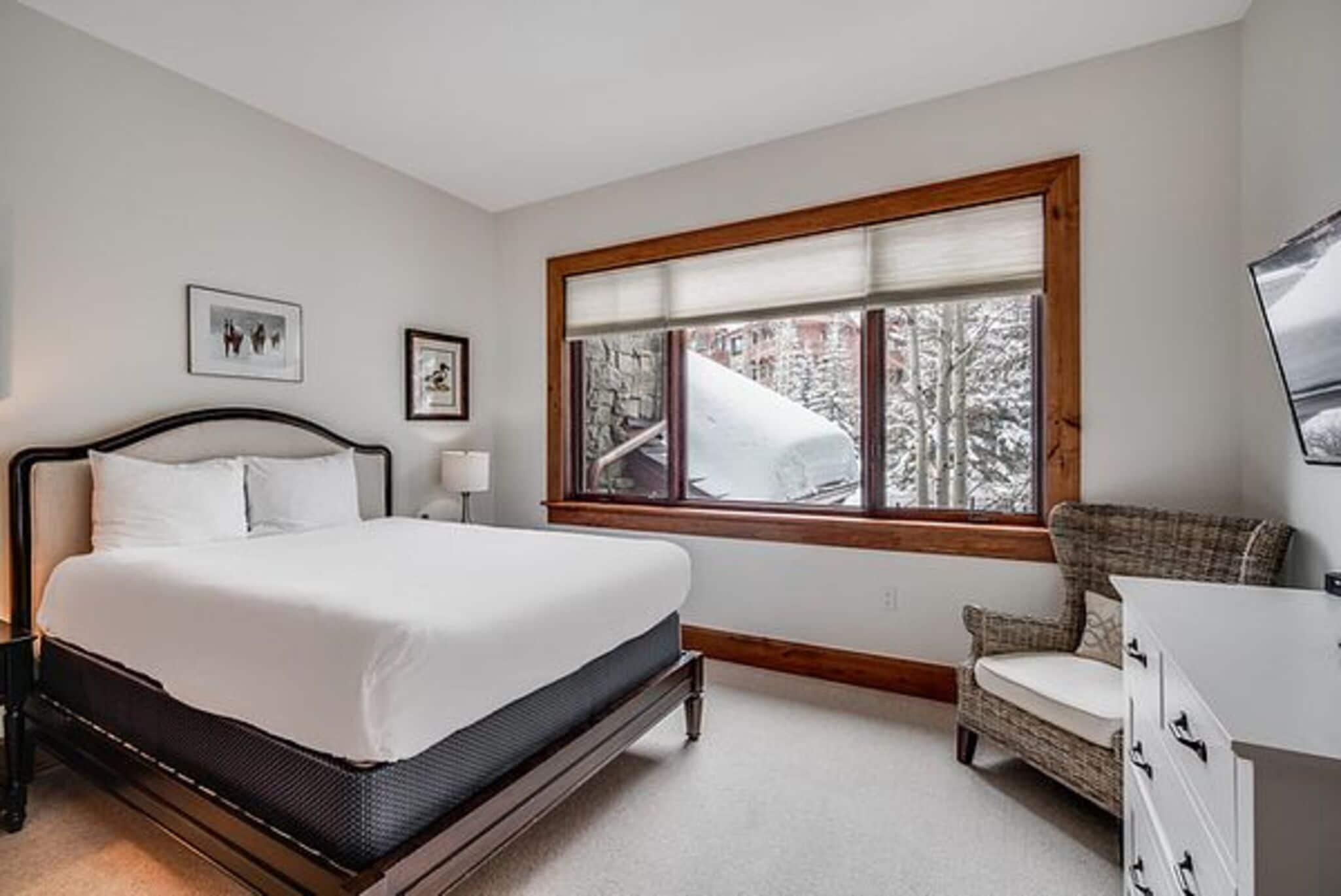 A bedroom with a bed, a chair, a dresser, a window with a view of trees, and two framed pictures on the wall.