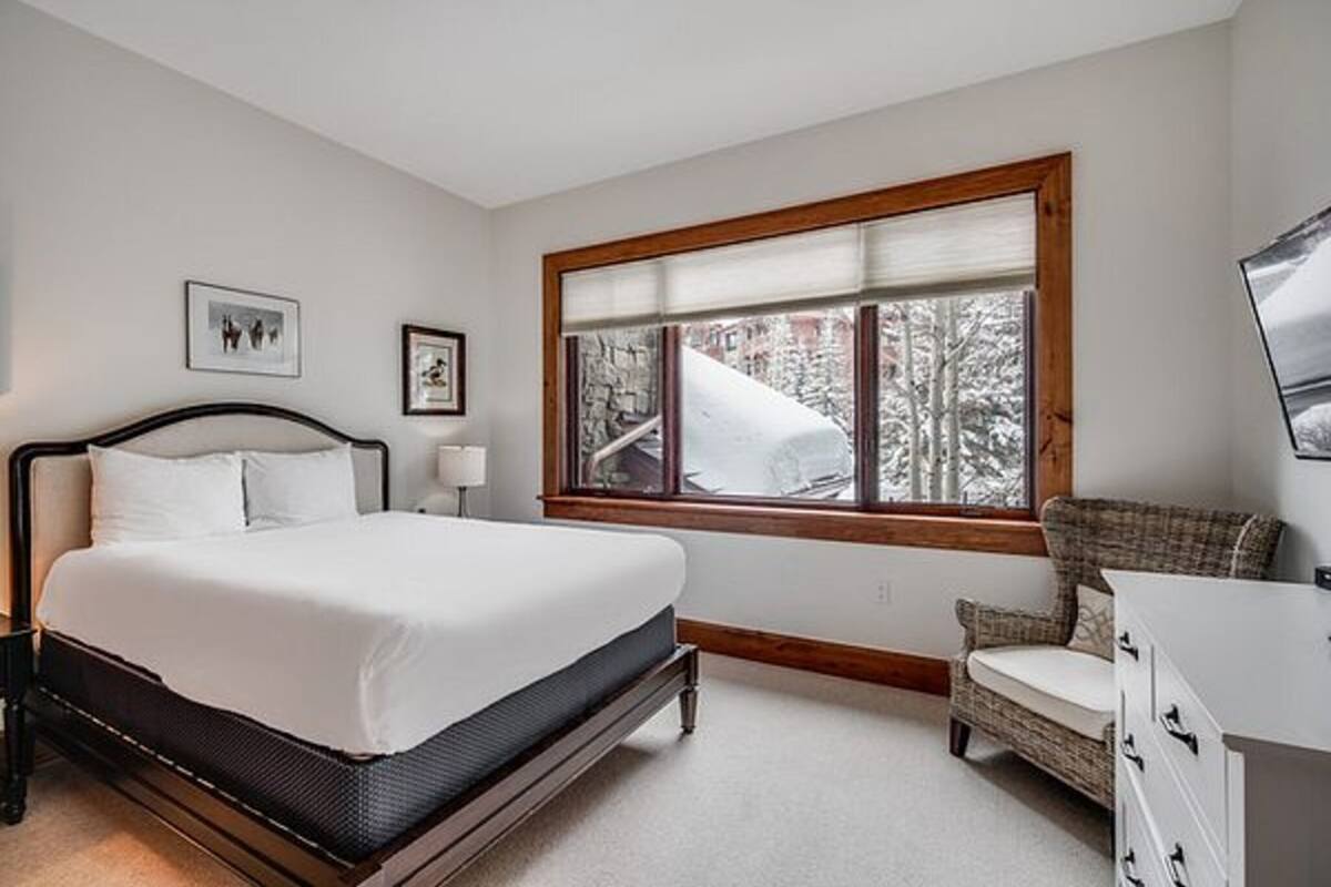 A bedroom with a bed, a chair, a dresser, a window with a view of trees, and two framed pictures on the wall.