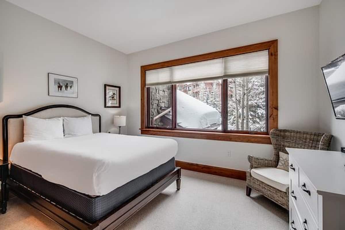 A bedroom with a bed, a chair, a dresser, a window with a view of trees, and two framed pictures on the wall.