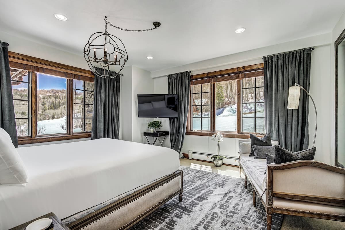 A bedroom with a large bed, a TV, a sofa, and a view of a snowy landscape.