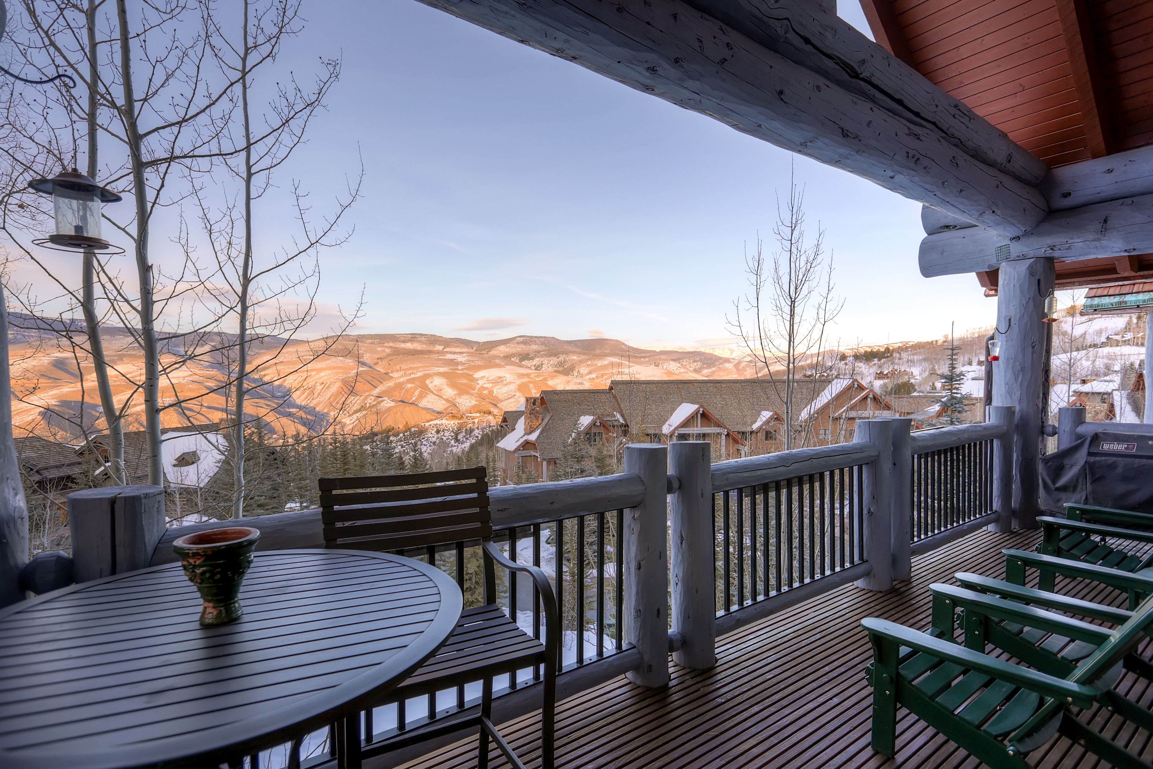 A wooden deck with a table and chairs, overlooking a mountainous landscape with snow-covered houses.