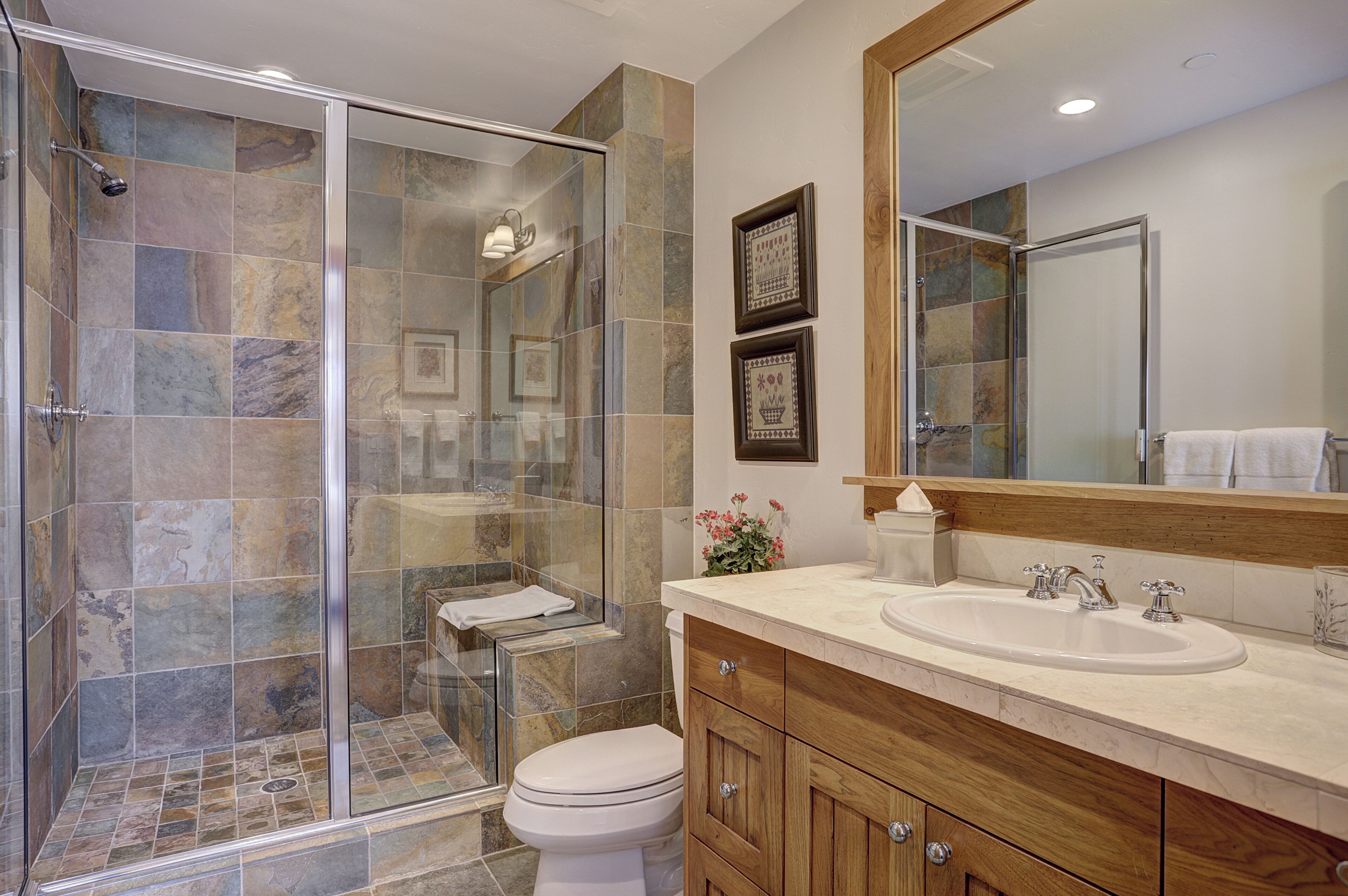 Un baño moderno con ducha de vidrio, un espejo grande y un mueble de tocador de madera.