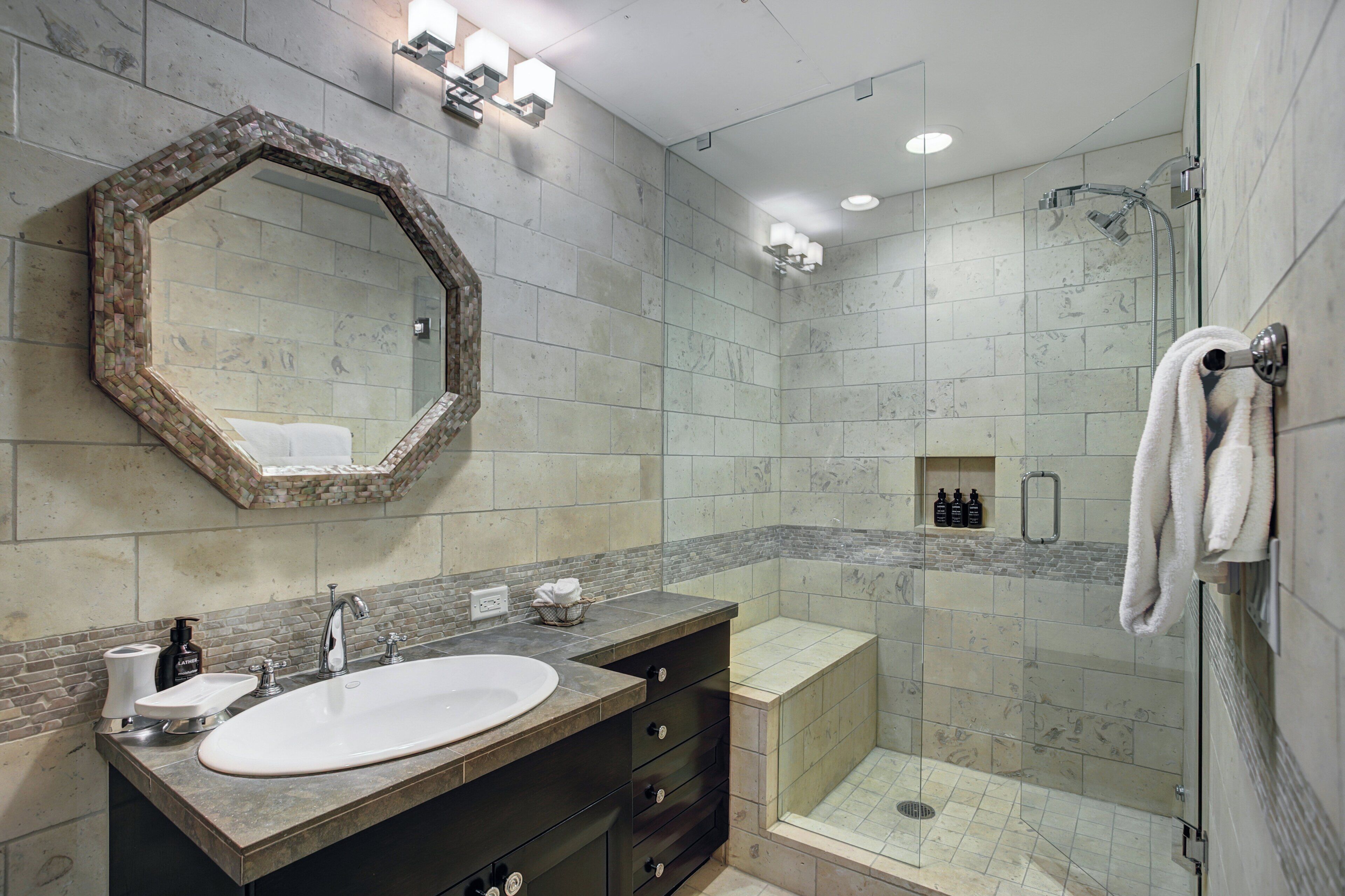 Ein modernes Badezimmer mit großem Spiegel, Waschbecken, Dusche und Handtuchhalter.