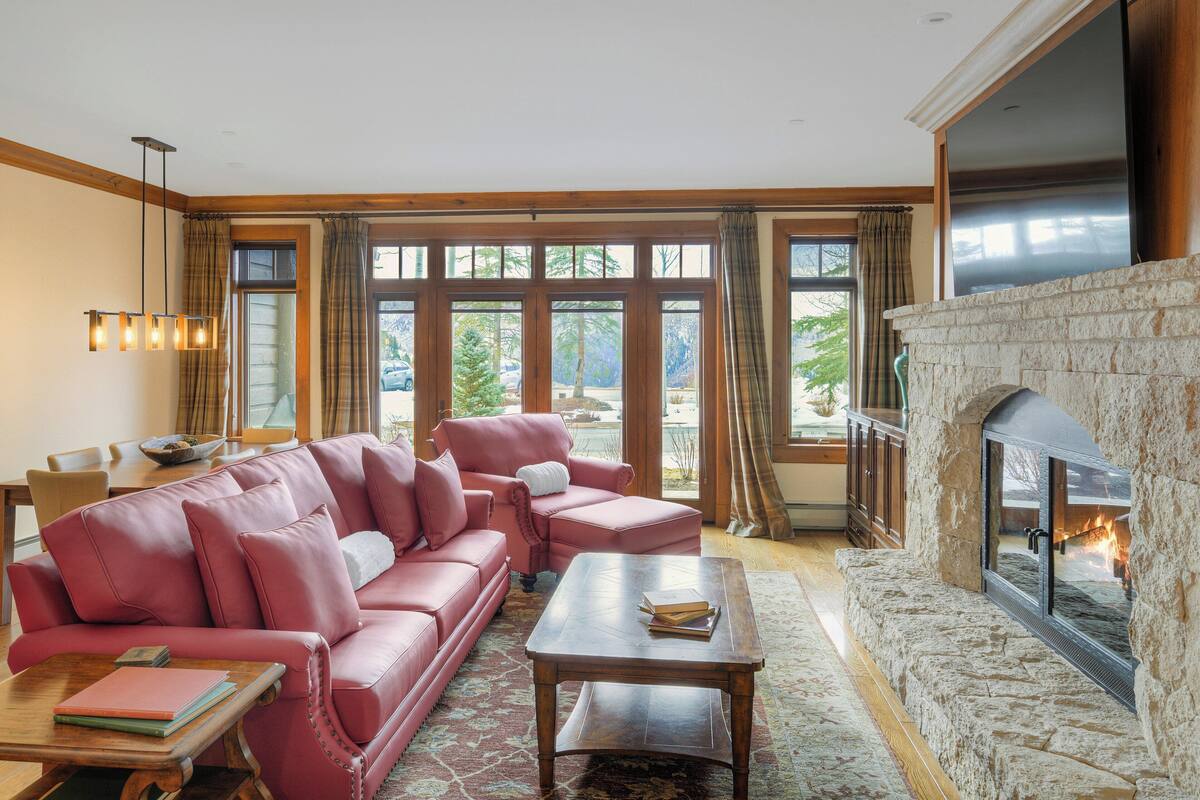 A living room with a stone fireplace, a pink sectional sofa, and a dining area with a table and chairs.