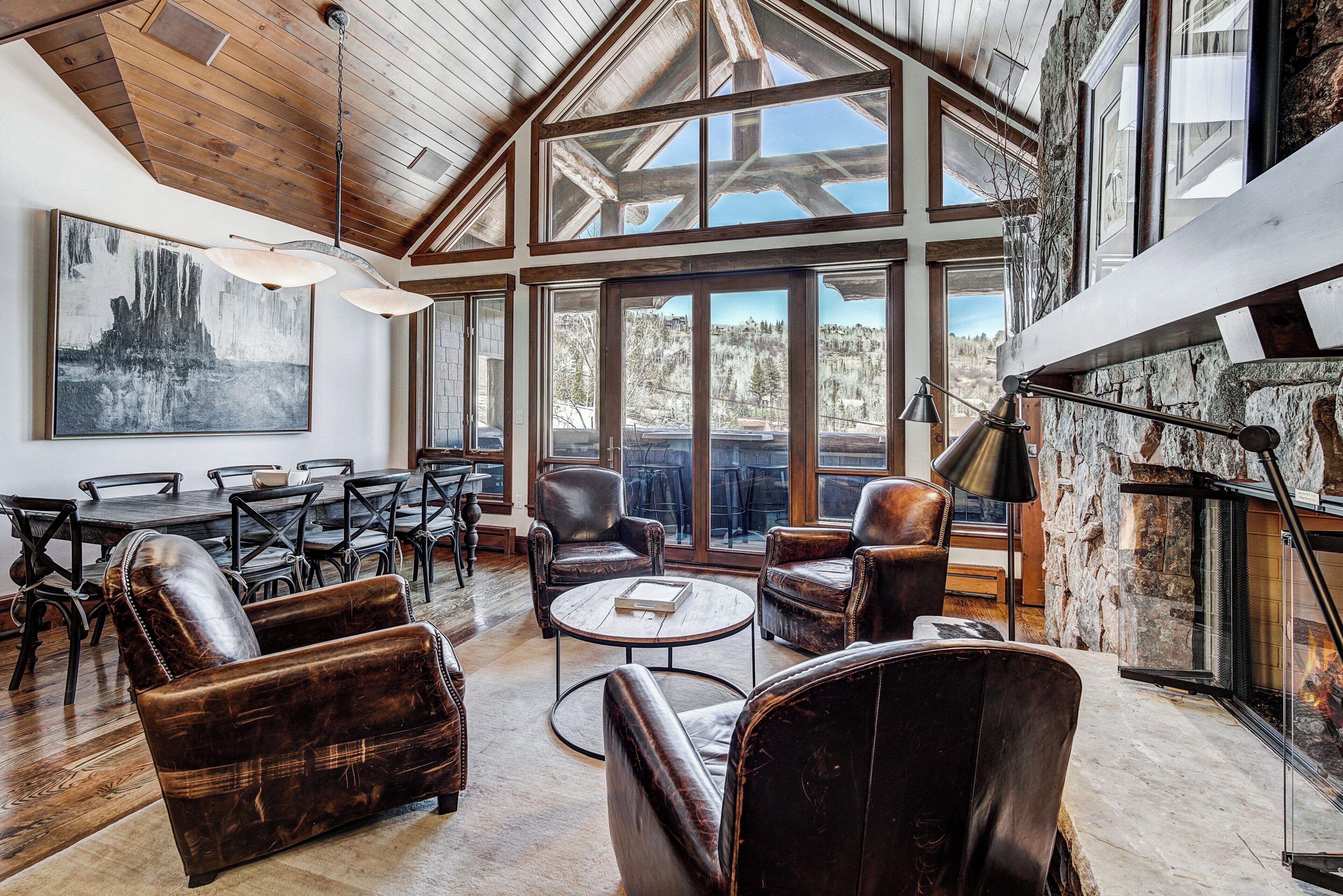 A spacious living area with leather sofas, a dining table, and chairs. Large windows offer a view of the outdoors.