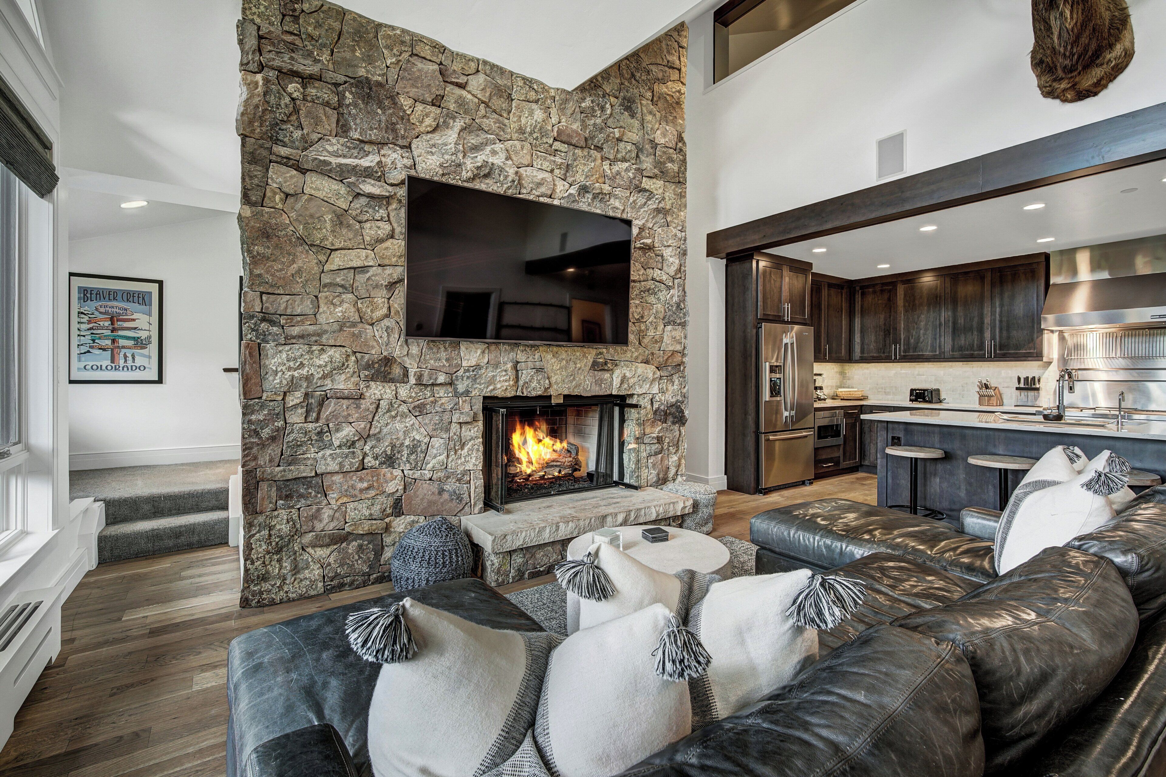 Una sala de estar moderna con chimenea de piedra, sofá de cuero y una zona de cocina al fondo.
