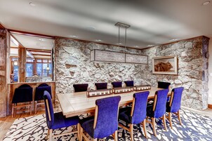 A dining area with a stone wall, a wooden table, and blue chairs.