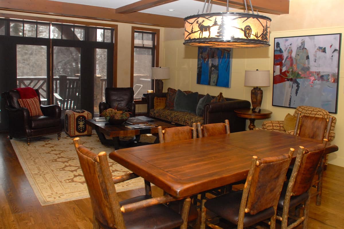 A spacious living room with a large wooden dining table, comfortable seating, and a chandelier.