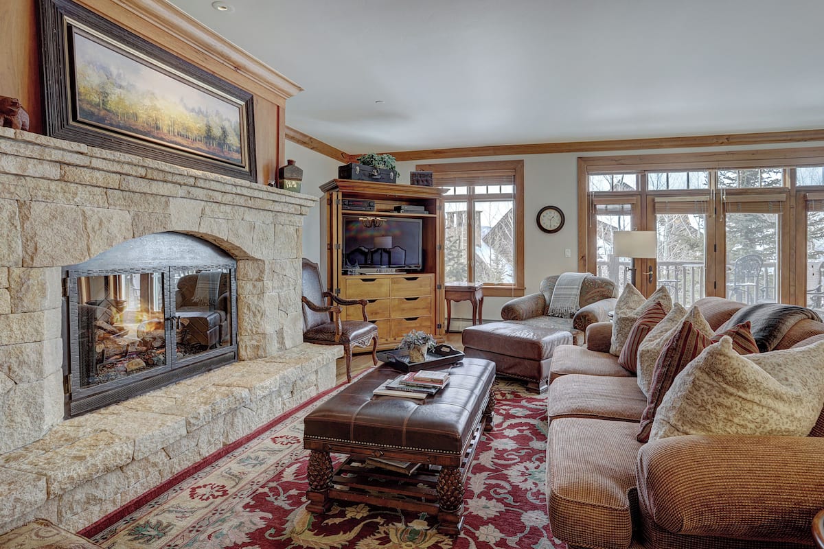 A cozy living room with a stone fireplace, comfortable seating, and a large window providing natural light.