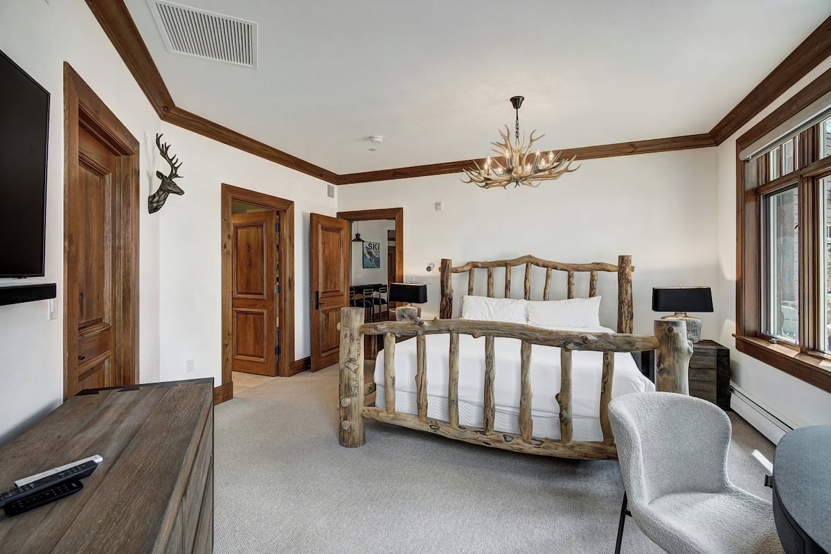 A bedroom with a rustic wooden bed frame, a chandelier, and a television on a wooden table.