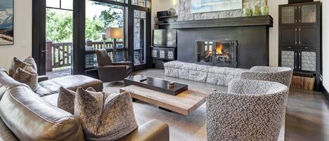A spacious living room with a stone fireplace, leather sofas, and a large window overlooking a deck.