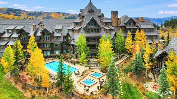 A large lodge with a central pool, multiple guest rooms, and a mountainous backdrop. - Bachelor Gulch Village by Vail Resorts (Avon)