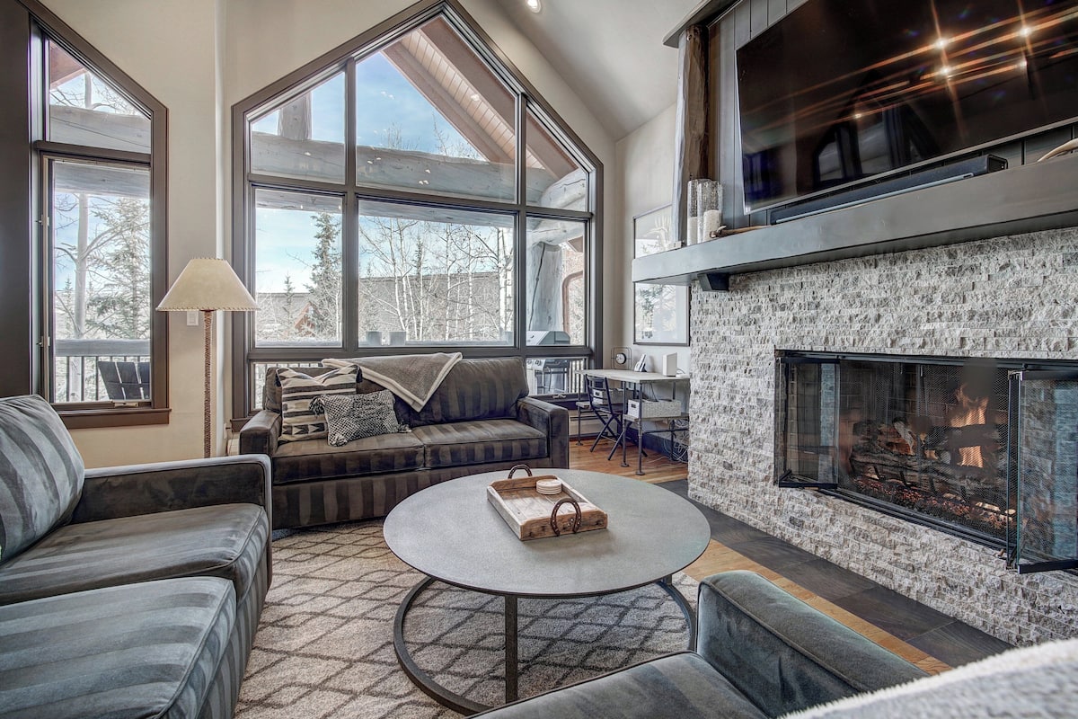 A spacious living room with a fireplace, large windows, and a cozy seating area.
