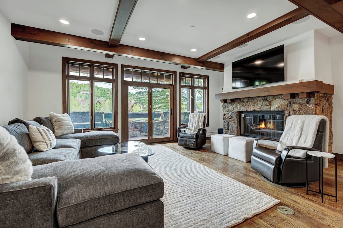 A modern living room with a stone fireplace, leather sofa, and large windows offering a view of the outdoors.